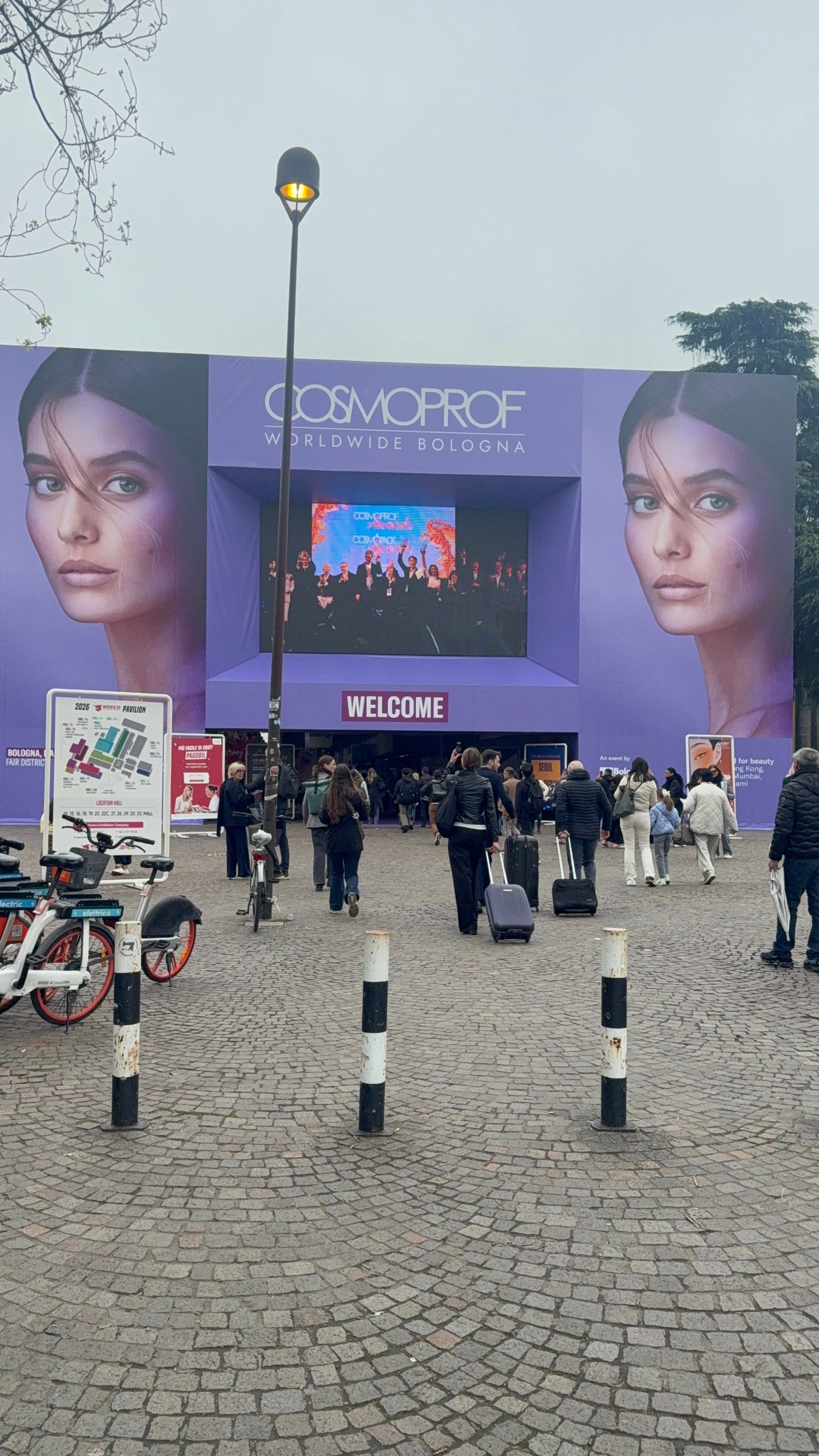 entrata cosmoprof bologna, porte viola, scritta cosmoprof in bianco e welcome in viola. persone davanti che stanno entrando nella fiera